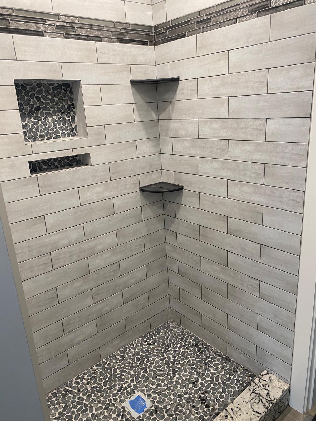 Grey subway tile shower stall with pebble mosaic floor and niches
