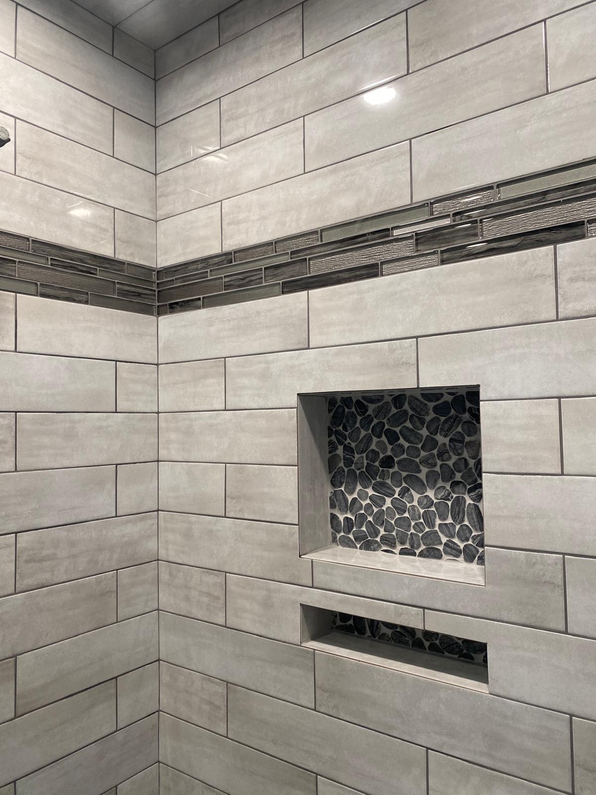 Grey subway tile shower with glass mosaic accent and pebble niche