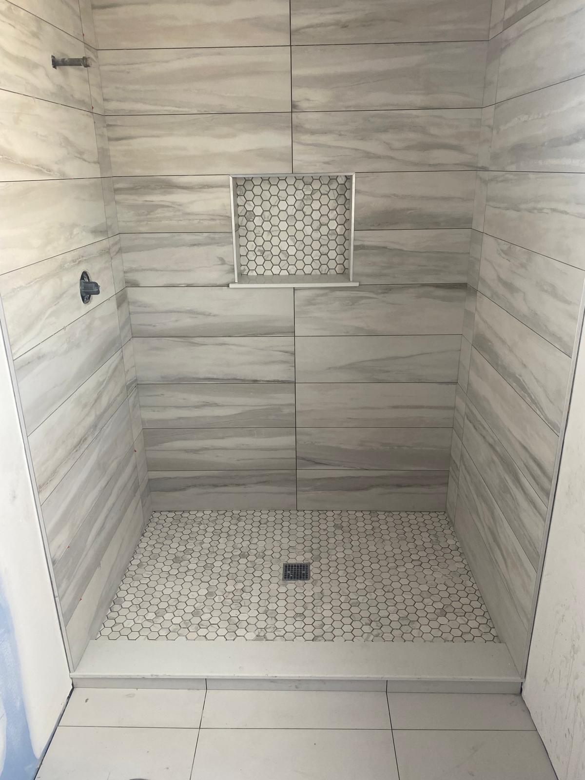 Grey marble-look tile shower with hexagon mosaic floor and niche